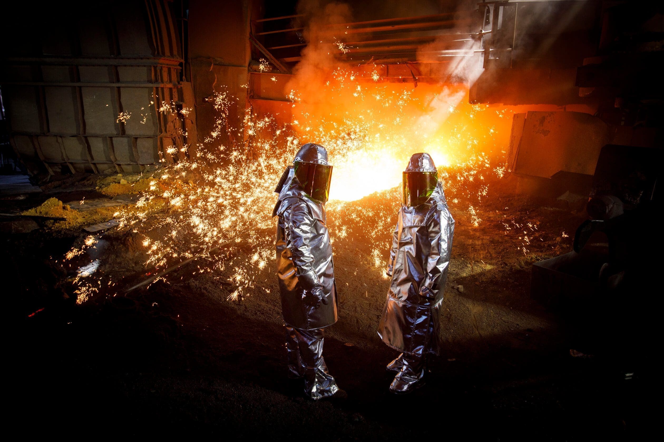 two people in protective suits and helmets standing in front of a fire